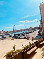 A marina with parked cars and boats, a clear sky, and buildings in the background.