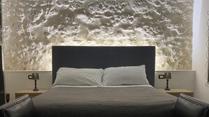 Ein Bett mit dunklem Kopfteil, zwei Nachttische und eine Wand mit strukturierter Oberfläche.