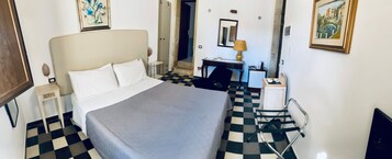 A hotel room with a large bed, a desk, a chair, and a checkered floor.