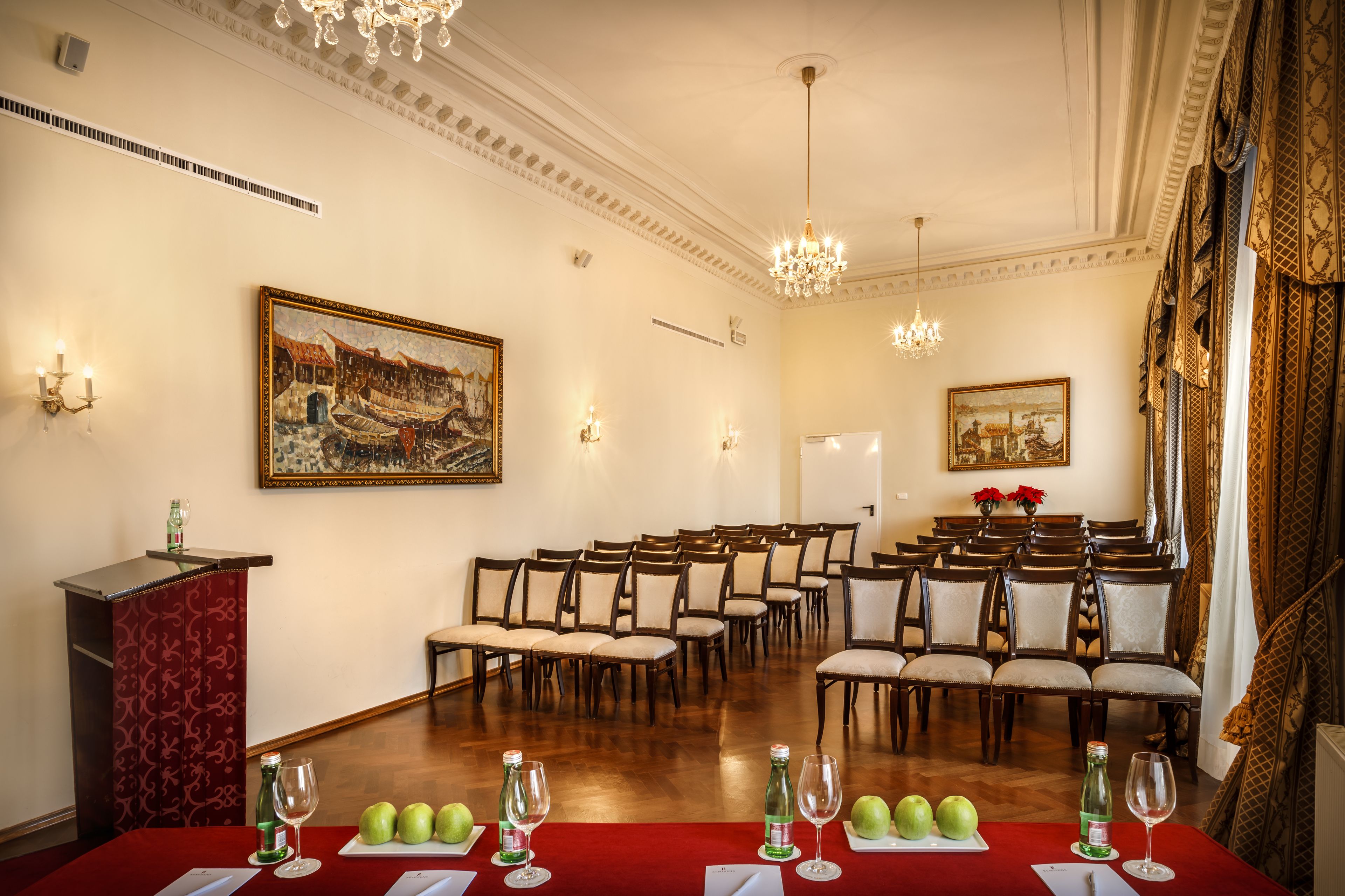 A conference room with rows of chairs, a podium, and a table with wine glasses and apples.