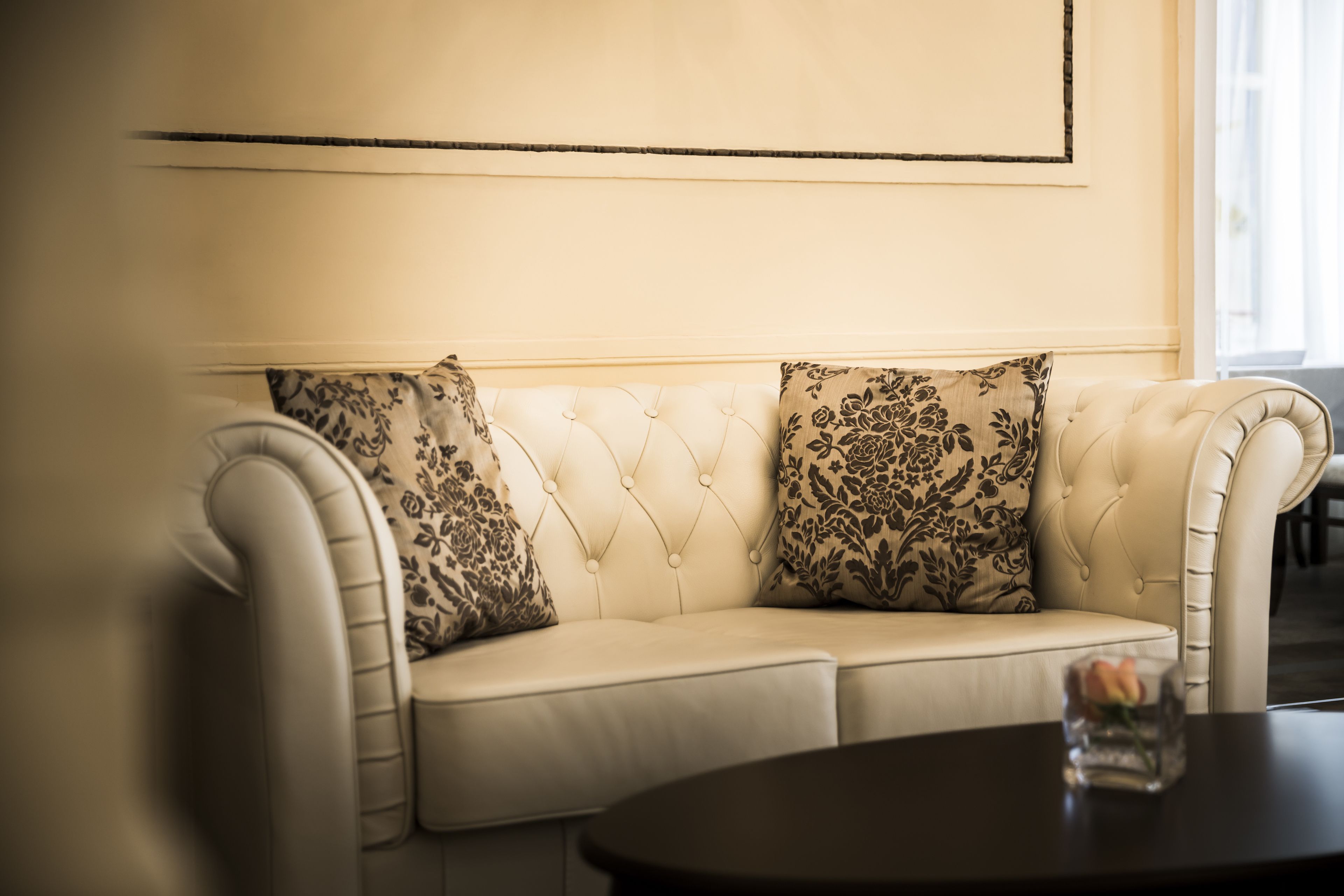 A cream-colored tufted sofa with floral-patterned cushions against a plain wall.