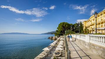 Eine Uferpromenade mit Steinbalustrade, Sitzgelegenheiten im Freien und Blick auf das Meer.