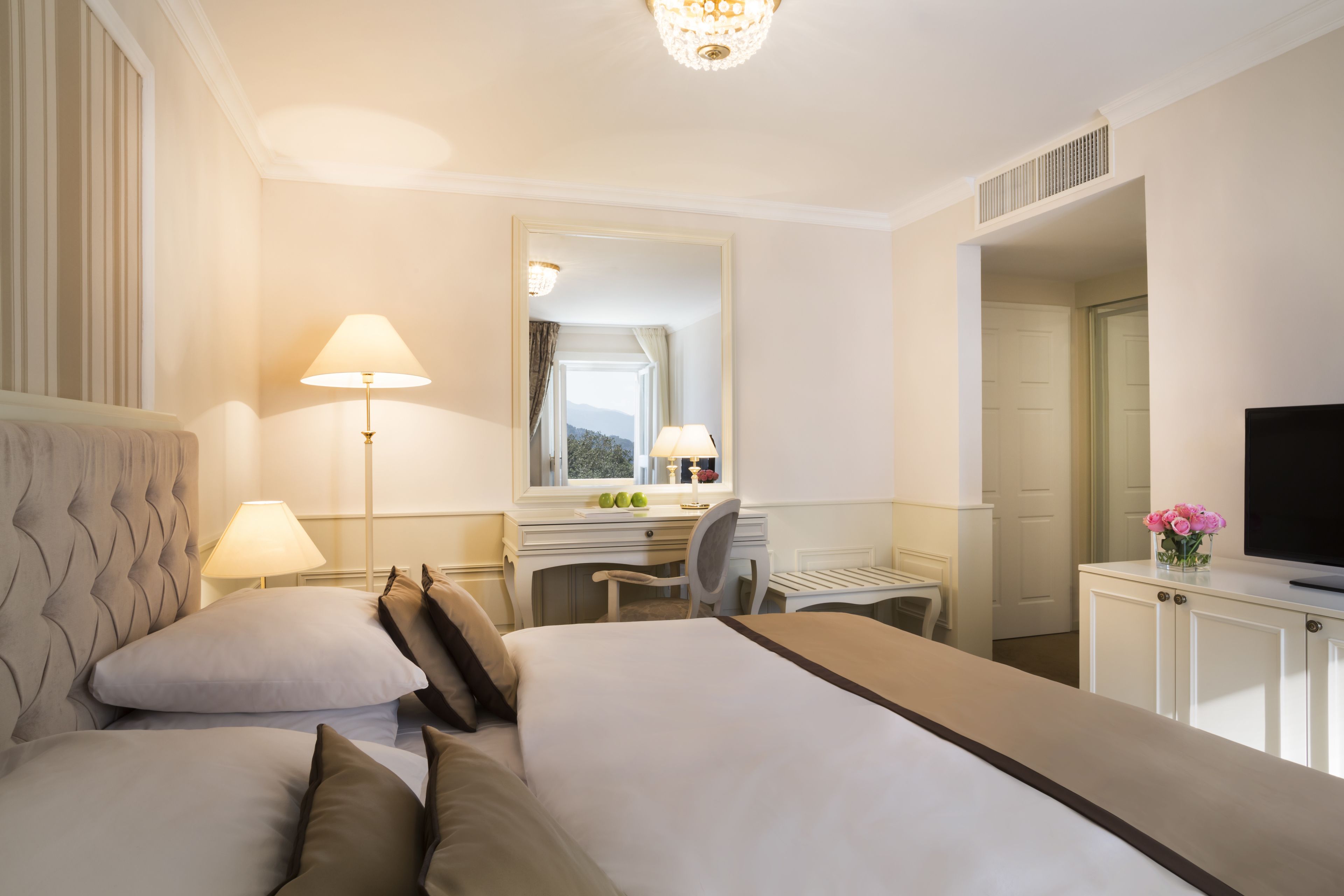 A hotel room with a large bed, a desk, a chair, a television, and a mirror.