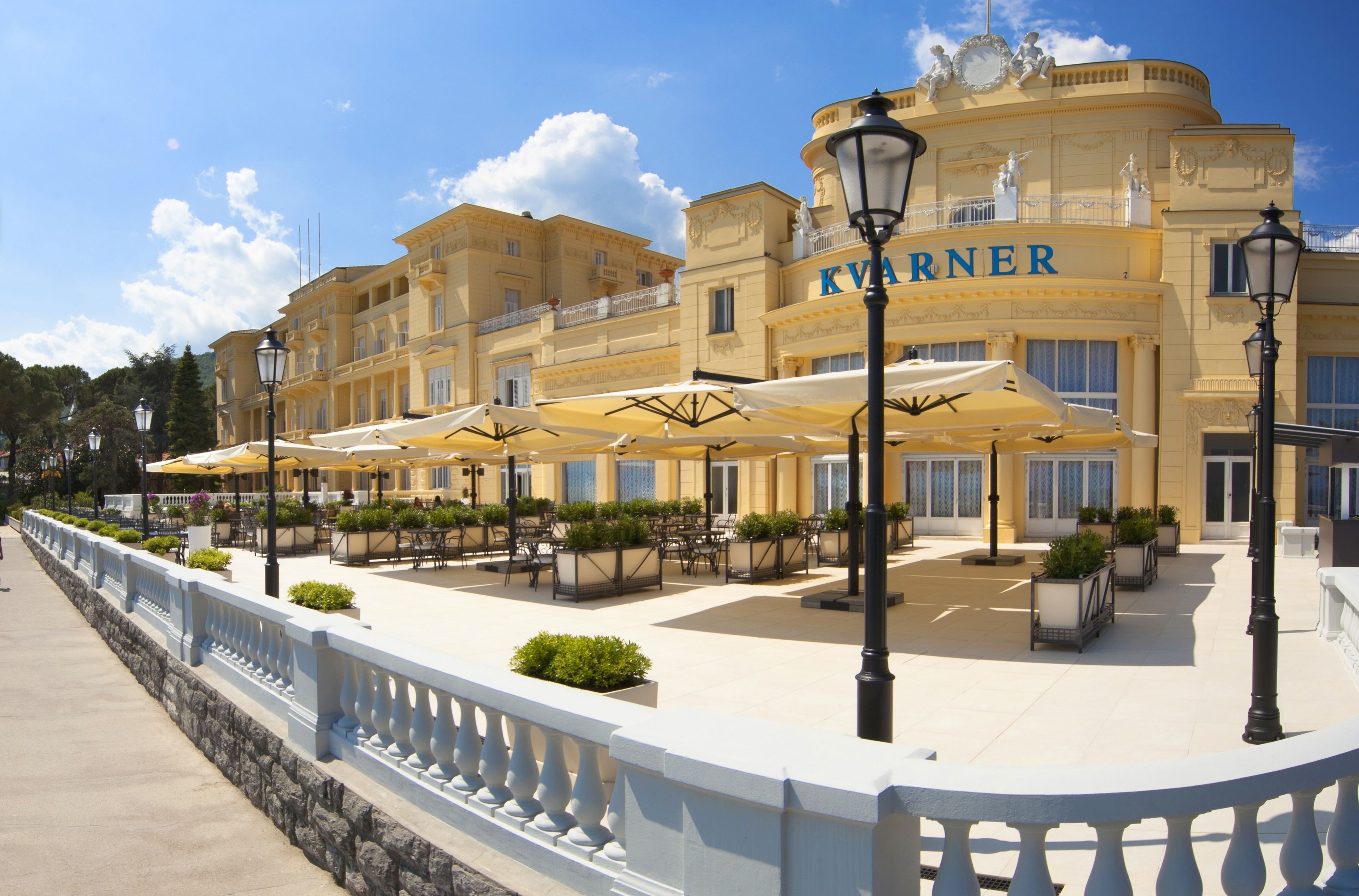 A hotel with outdoor seating, a white balcony railing, and a sign that reads "KVARNER".