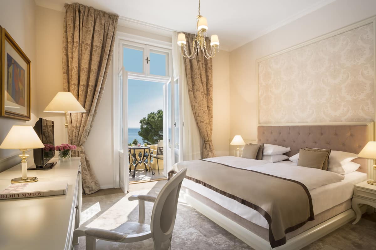 A well-appointed bedroom with a large bed, two bedside tables with lamps, a chair, and a view of the outdoors.