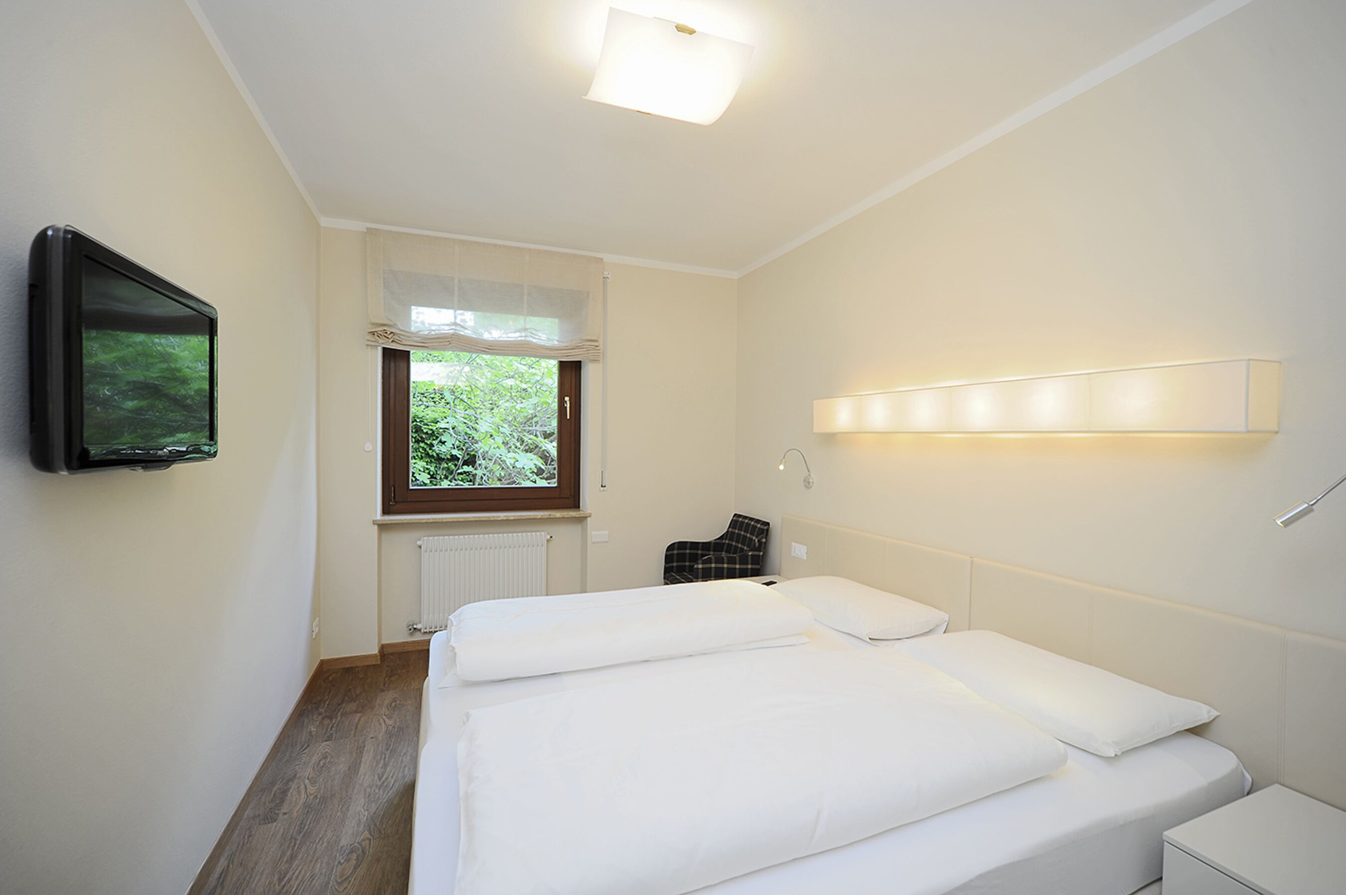 Habitación de hotel con dos camas, televisión, ventana con vistas a zonas verdes y una lámpara de noche.