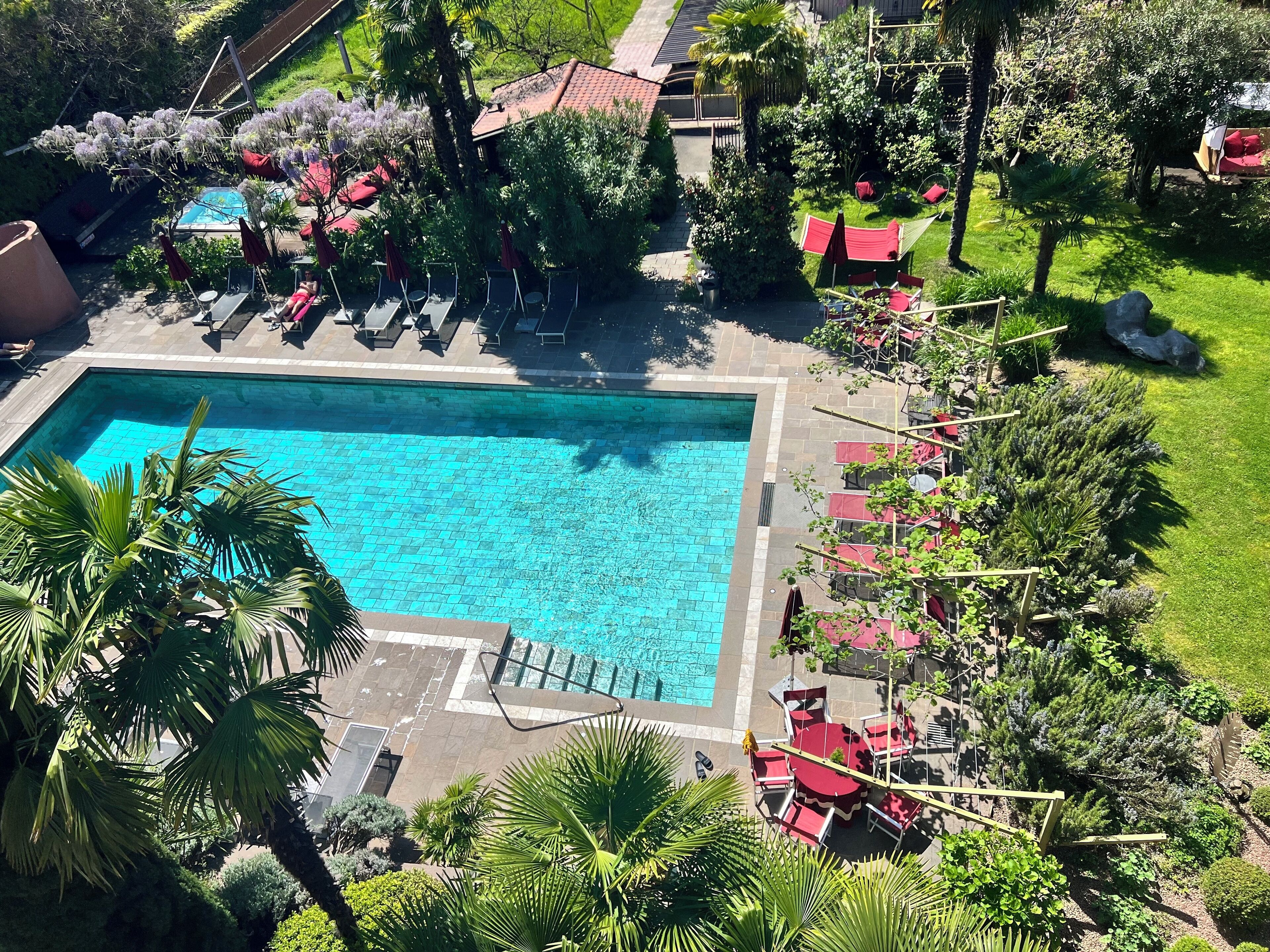 An aerial view of a hotel with a swimming pool surrounded by red umbrellas and lounge chairs.