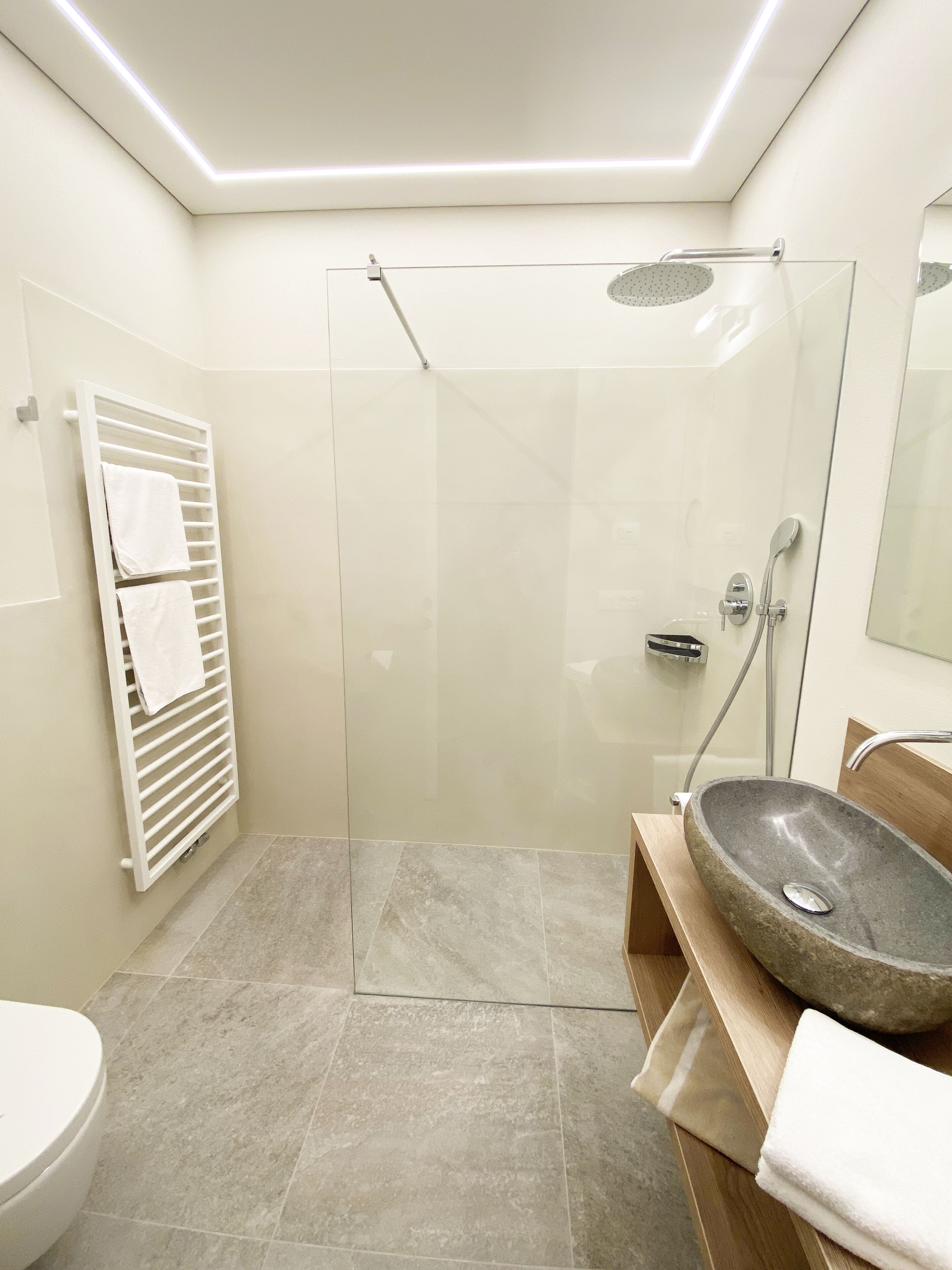 A modern bathroom with a glass shower enclosure, a stone sink, and a white towel rack.