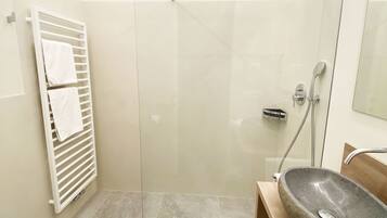 A modern bathroom with a glass shower enclosure, a stone sink, and a white towel rack.
