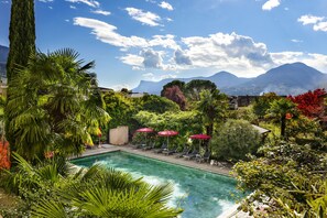 Un área de piscina con sillones y sombrillas, rodeada de exuberante vegetación y montañas al fondo.