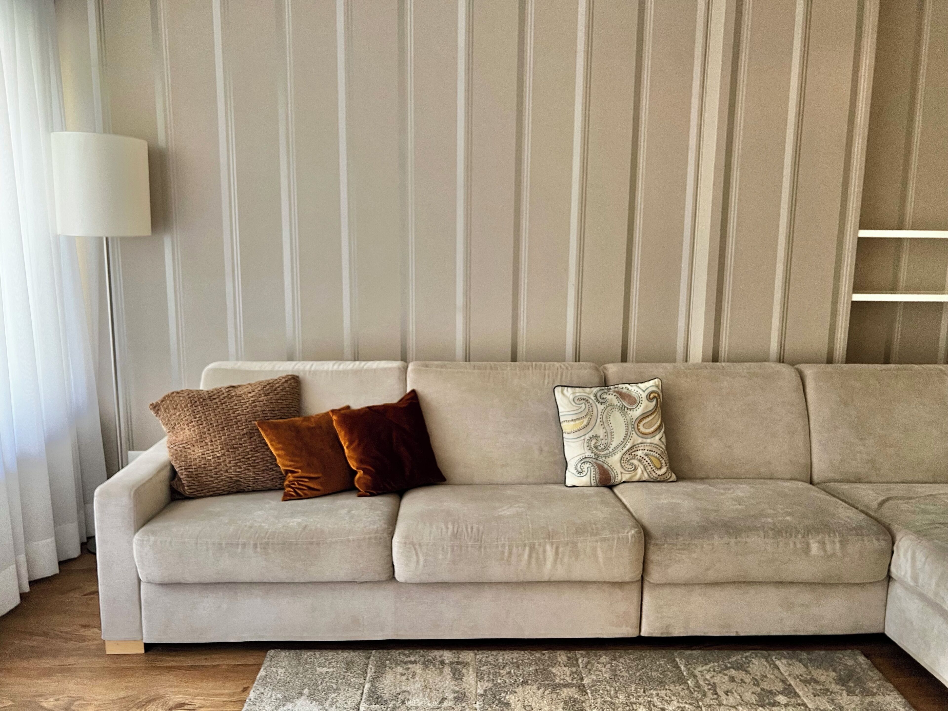 A beige sofa with three cushions against a striped wallpaper backdrop.