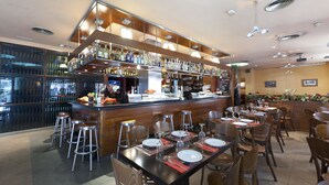 Un restaurante con zona de bar, varias mesas dispuestas para comer y una variedad de botellas en estanterías.