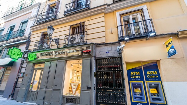 Una farmacia con un amplio escaparate de vidrio y una puerta metálica cerrada.