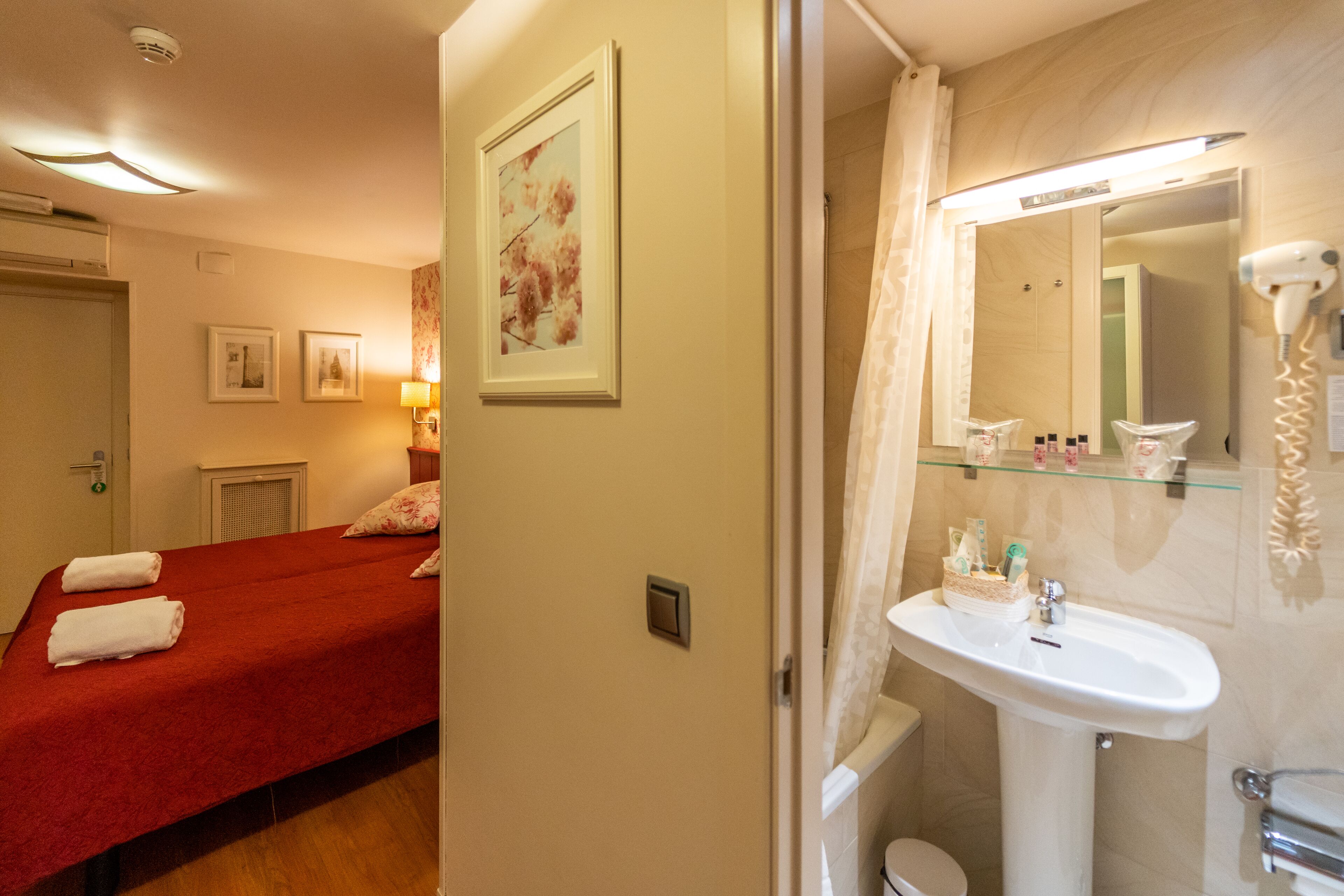 A hotel room with a bed, a bathroom with a sink and mirror, and a shower.
