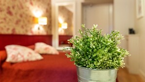 Habitación de hotel con cama, planta en maceta y pared roja.