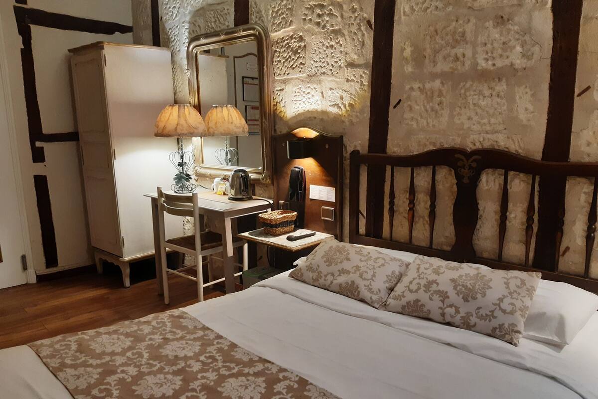 A bedroom with a bed, a desk with a lamp, a mirror, and a wooden headboard.