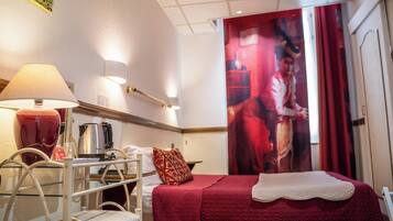 Una camera d'albergo con un letto, una scrivania con una lampada, una sedia e un grande quadro appeso al muro.