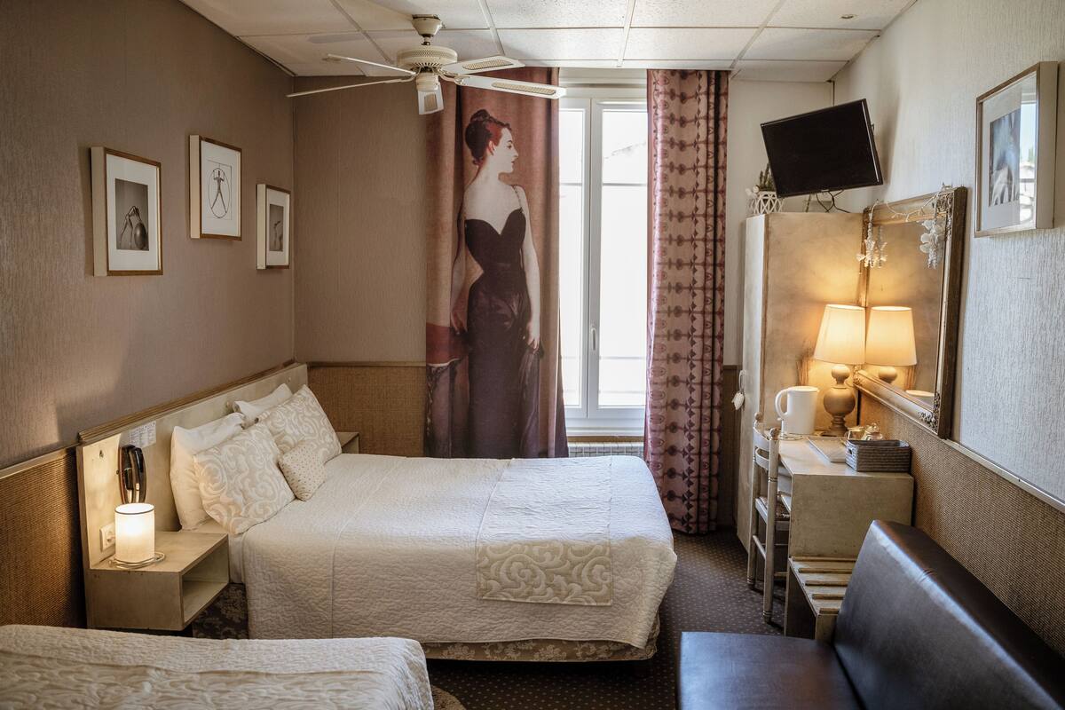 A hotel room with a bed, bedside table, lamp, TV, and a large mirror.