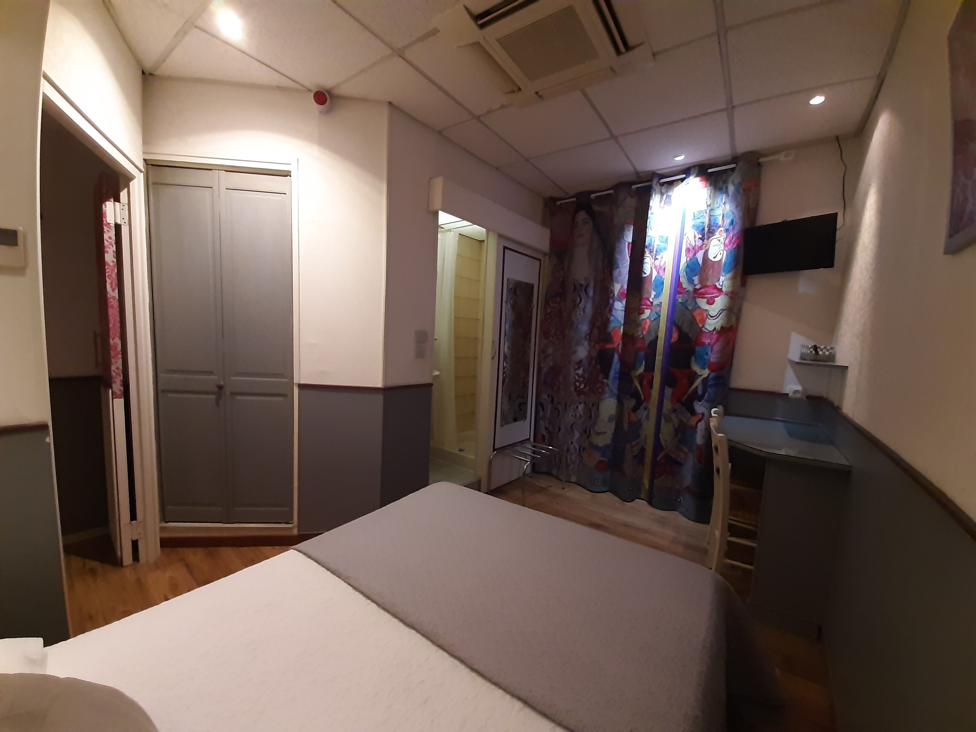 A bedroom with a bed, a desk, a wardrobe, and a shower area.