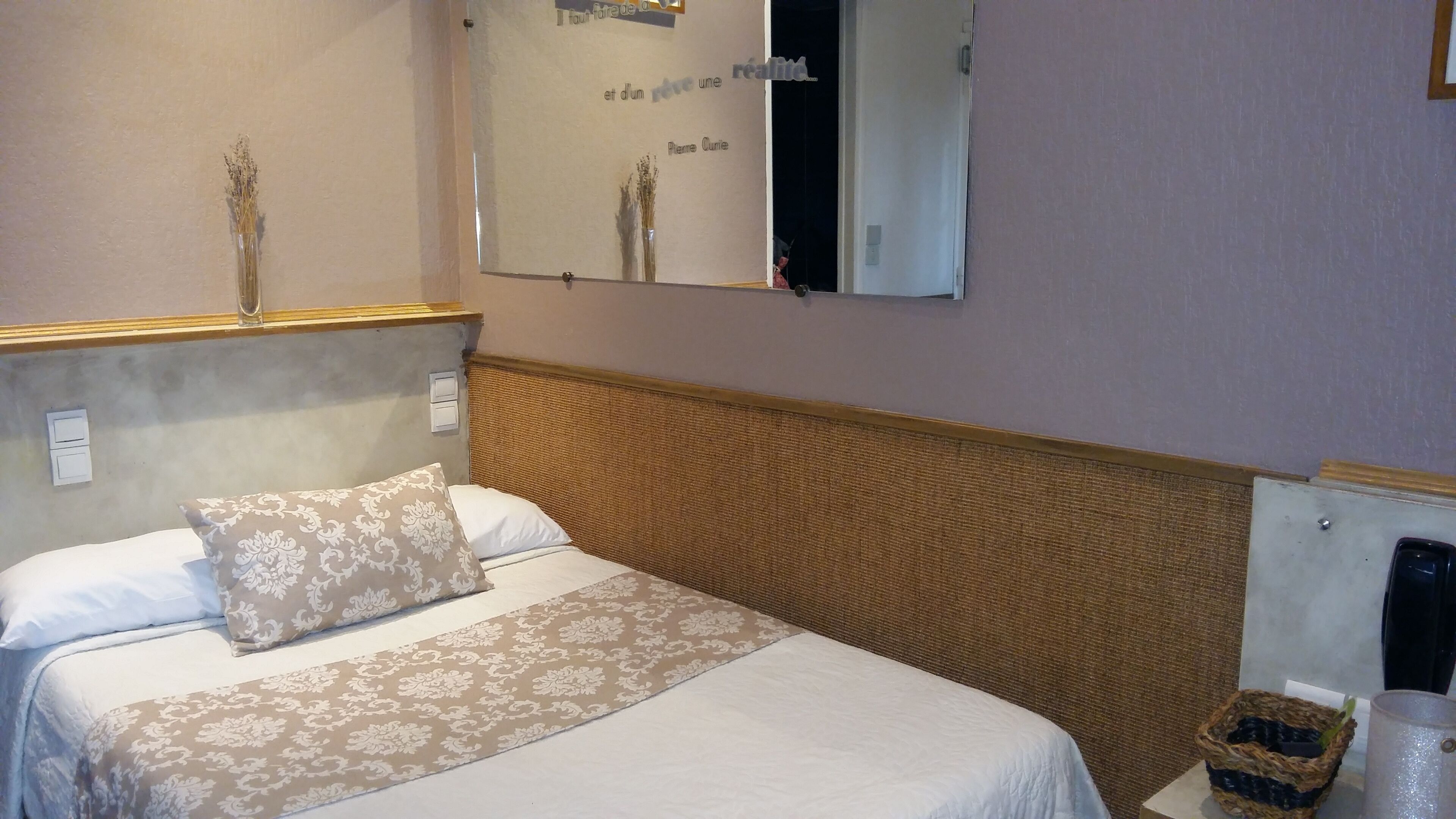 Une chambre d’hôtel avec un lit, une table de chevet avec une lampe, un miroir et un mur orné d’une citation.