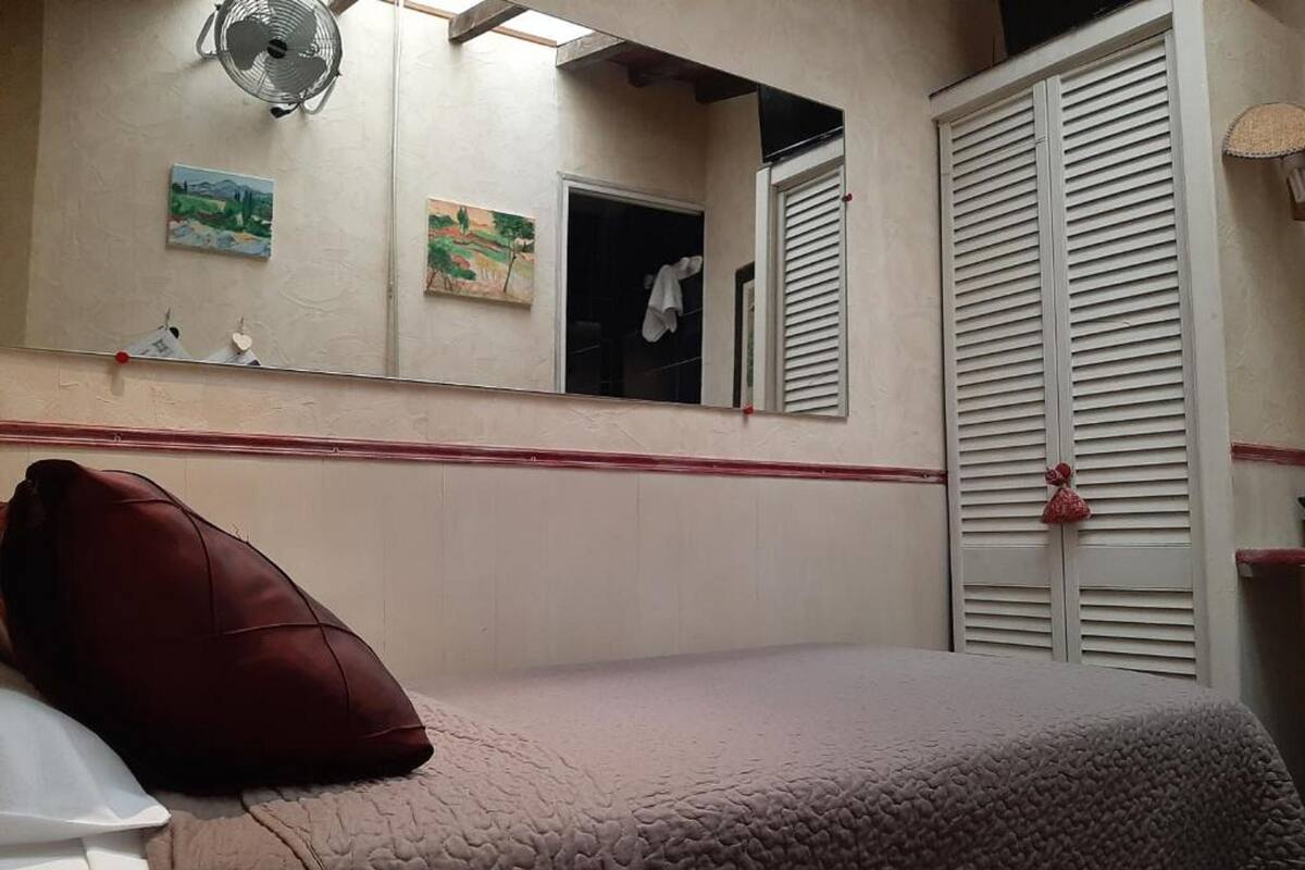 A bedroom with a bed, a pillow, a mirror, and a window with shutters.