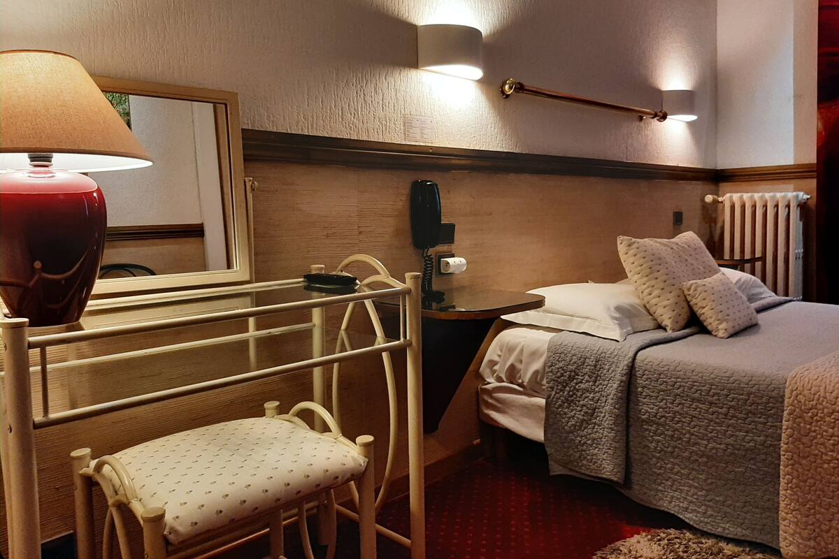 A hotel room with a bed, bedside table, lamp, chair, and a mirror.