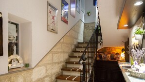 Una escalera con escalones de madera y barandal negro que lleva a una plataforma con una pequeña mesa y una planta en maceta.