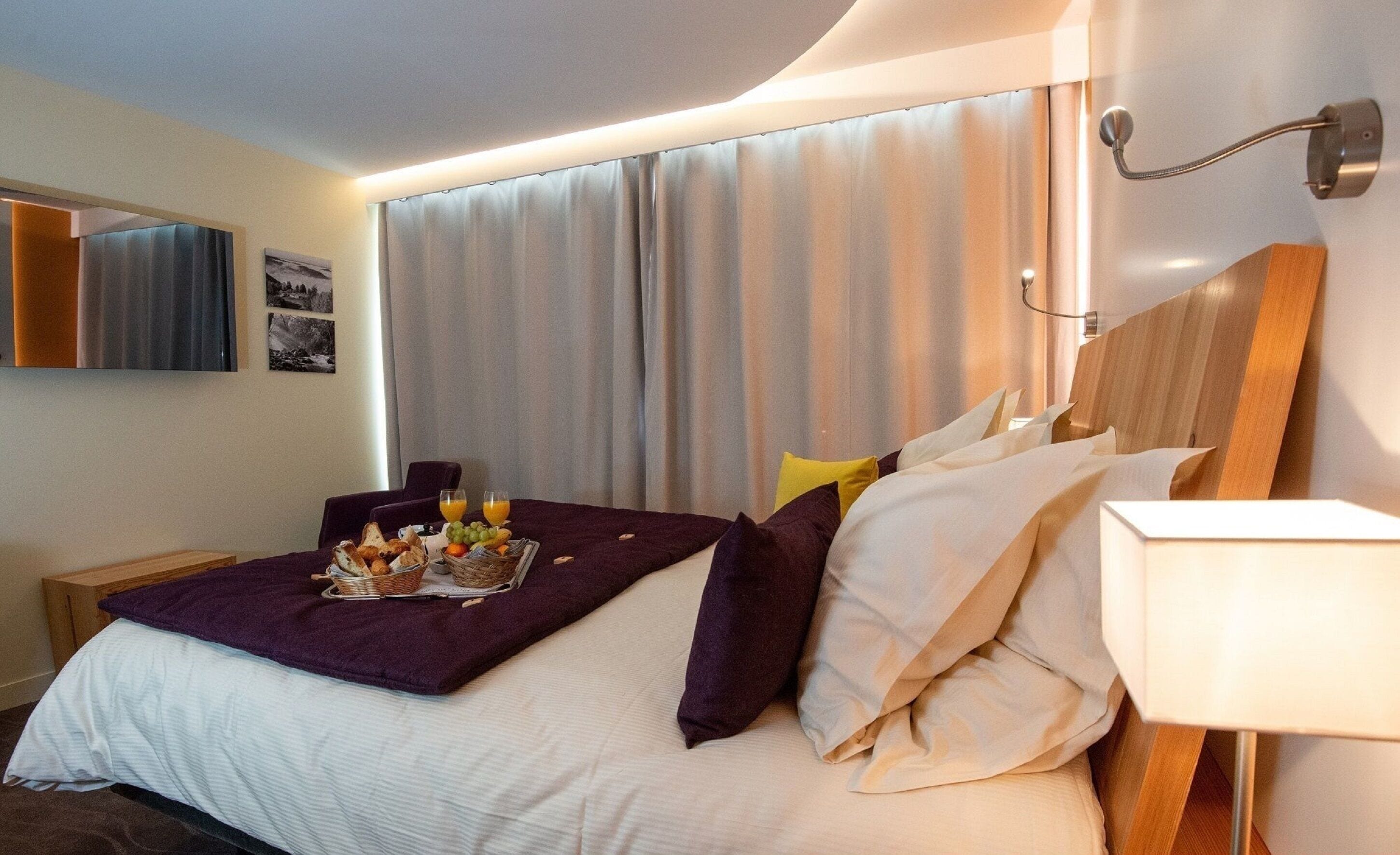 A hotel room with a neatly made bed, a side table with a lamp, and a breakfast tray on the bed.