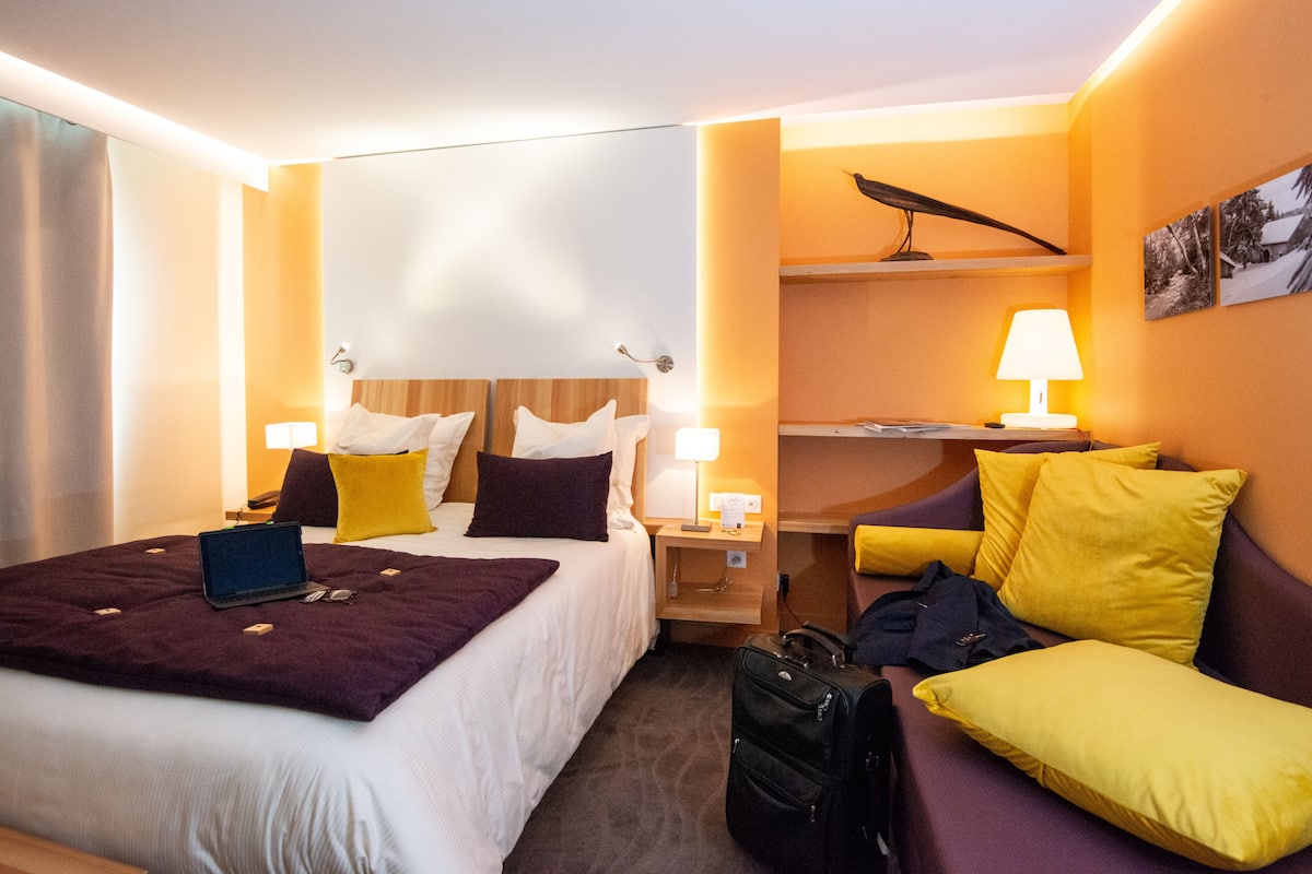 A hotel room with a bed, bedside tables, a desk, a chair, and a lamp.