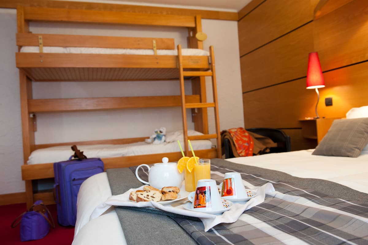 A hotel room with a bunk bed, a bedside table with a lamp, and a tray with breakfast items.