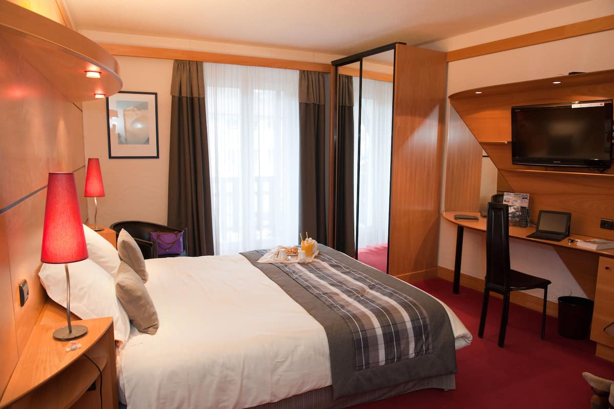 A hotel room with a bed, a desk with a laptop, a TV, and a red carpet.