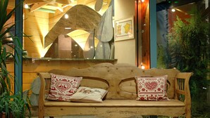 A wooden bench with two decorative pillows, positioned in front of a wooden wall with a large mirror and framed artwork. - Hôtel Les Vallées (La Bresse)