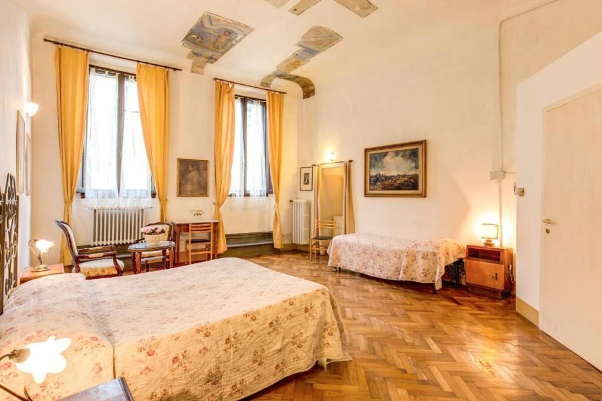 A room with two beds, a radiator, a desk with a chair, and a painting on the wall.