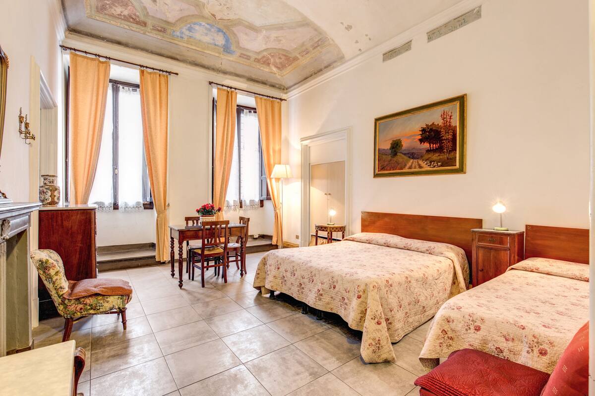 A hotel room with two beds, a dining area, and a painting on the wall.