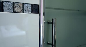 A bathroom with a glass shower door and a tiled backsplash. - Hotel Briand devient Hotel IPL (Levallois-Perret)