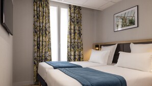 Habitación de hotel con dos camas, cortinas florales, un cuadro en la pared y suelo de madera.