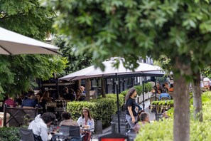 An outdoor café with tables and chairs, surrounded by greenery and umbrellas. - Hotel Charlemagne (Neuilly-sur-Seine)