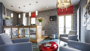 Un moderno vestíbulo de hotel con paredes grises de diseño, un mostrador de recepción, sofás grises, un objeto decorativo rojo y una araña.