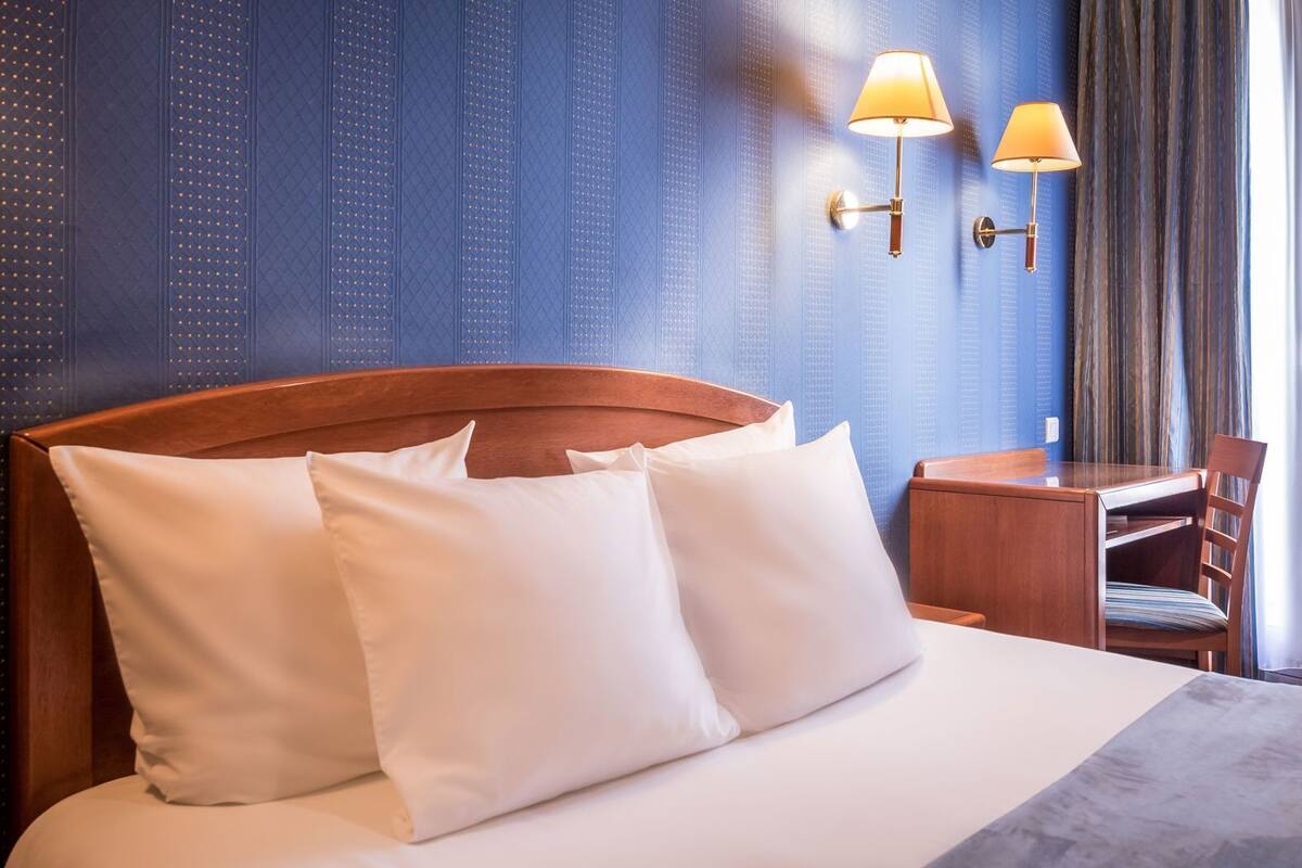 A hotel room with a bed, two bedside lamps, a desk, and a chair.