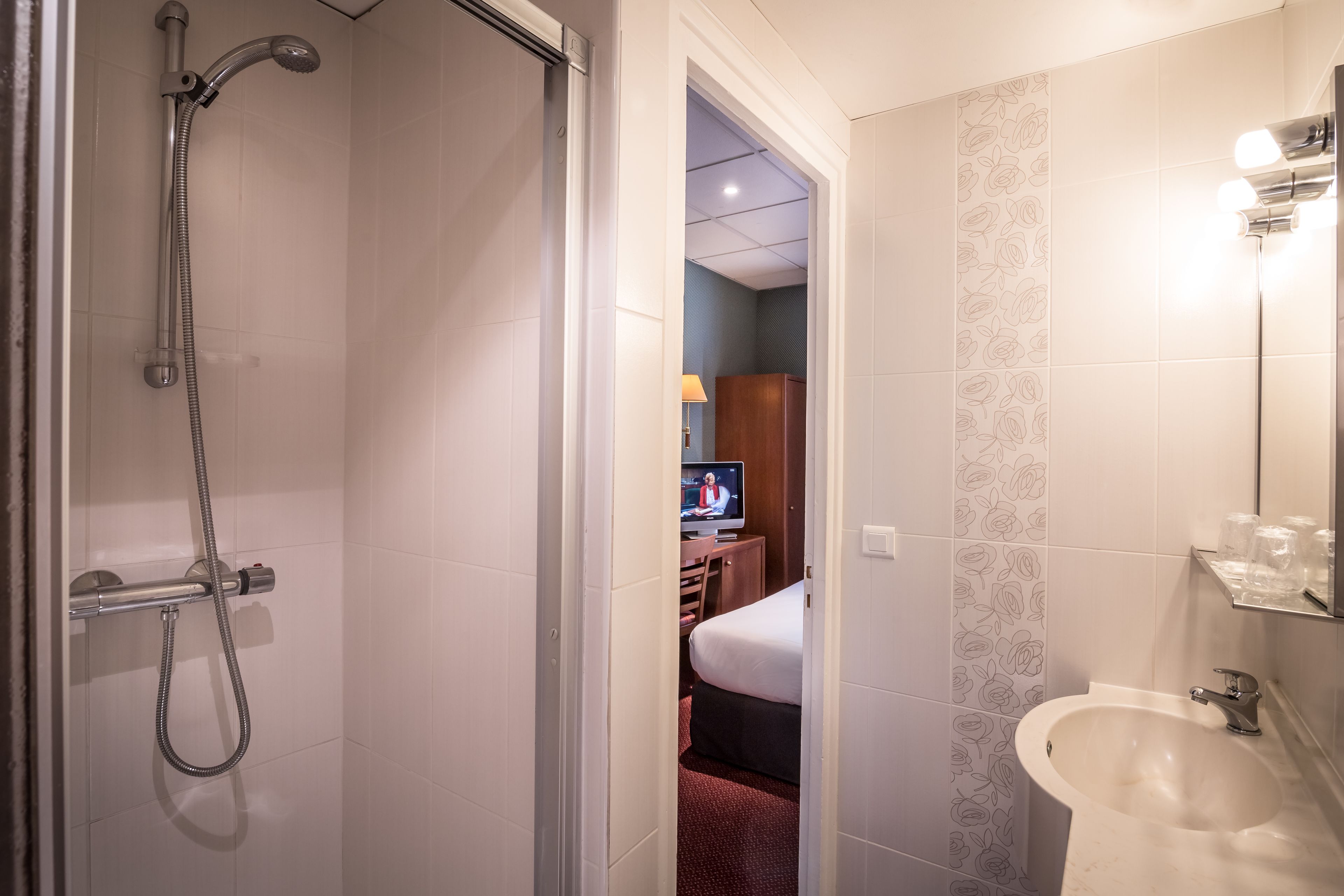A hotel bathroom with a shower, a sink, and a television in the adjacent room.