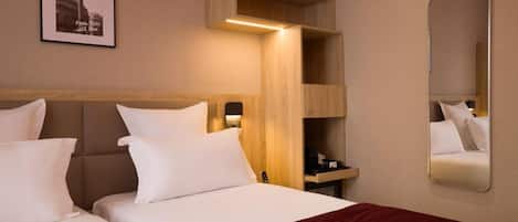A hotel room with two beds, a wooden headboard, a bedside table with a lamp, a mirror, and a framed picture on the wall.