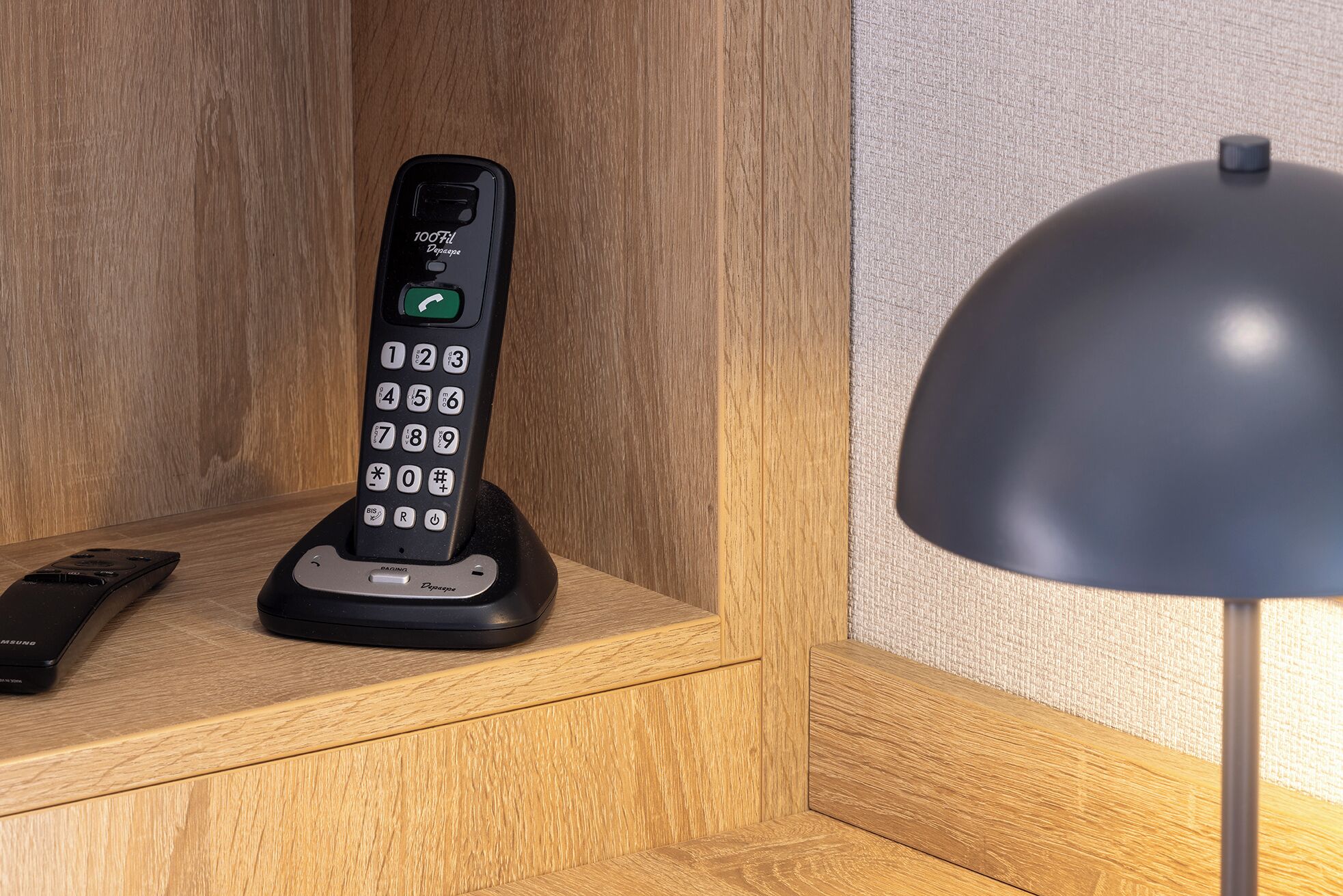 Un téléphone modèle 100 posé sur un bureau en bois, avec une lampe.
