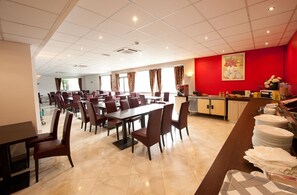 A spacious dining area with multiple tables and chairs, a kitchen counter with dishes, and a red accent wall. - Hotel Milton (ex Gis Hotel) (Neuilly-Plaisance)