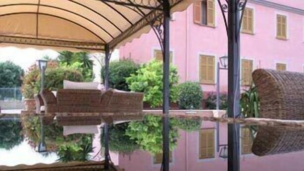 A covered outdoor seating area with a reflective surface, a brick bench, and a pink building in the background. - Arco di Travertino (Rome)