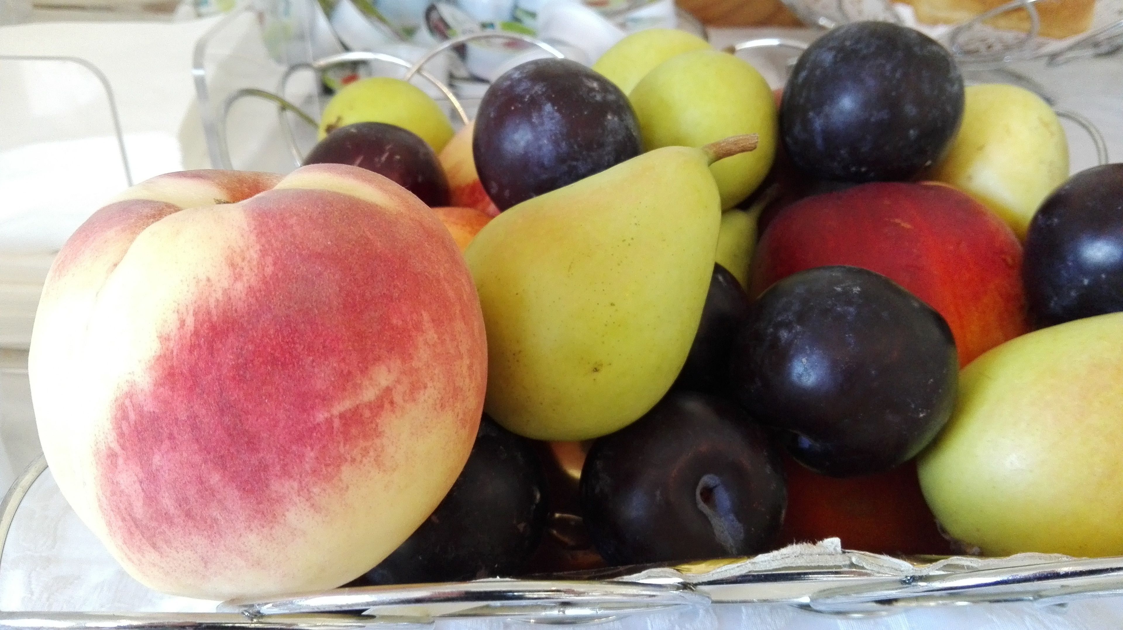 Een schaal met een verscheidenheid aan fruit, zoals perziken, pruimen en peren.