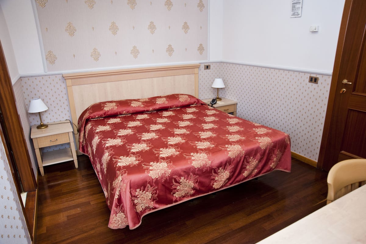Un dormitorio con cama, mesita de noche, silla y puerta.