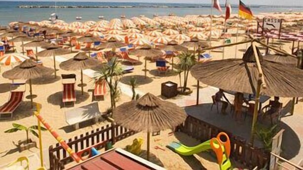 A beach with numerous umbrellas and beach chairs, a lifeguard tower, and flags. - Alba d'Oro (Bellaria-Igea Marina)