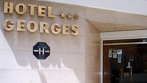 Ein Hotel Eingang mit der Aufschrift "HOTEL GEORGES" in großen Lettern und einem Schild, das einen barrierefreien Zugang kennzeichnet.