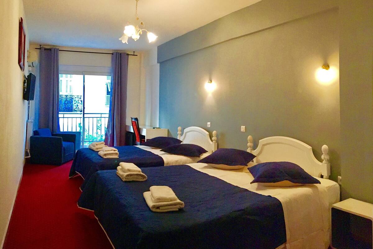 Une chambre d’hôtel avec deux lits, une moquette rouge, un balcon et une tête de lit blanche.
