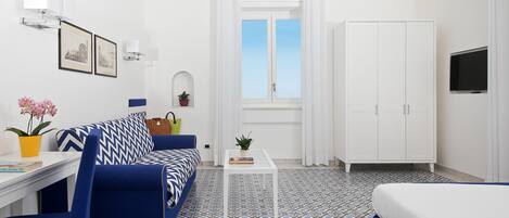 A room with a bed, a sofa, a small table, a TV, a wardrobe, and a window with curtains.